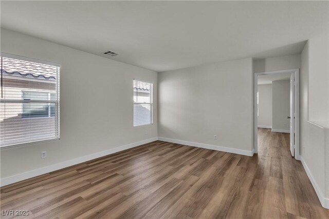 spare room with baseboards, visible vents, and wood finished floors