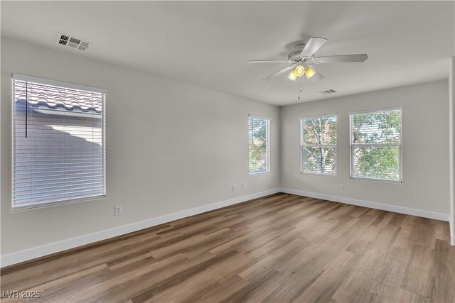 empty room featuring plenty of natural light, wood finished floors, and visible vents