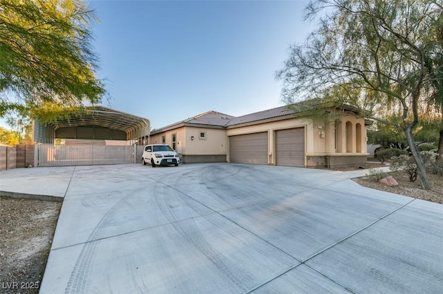 exterior space featuring stucco siding, concrete driveway, an attached garage, fence, and a carport