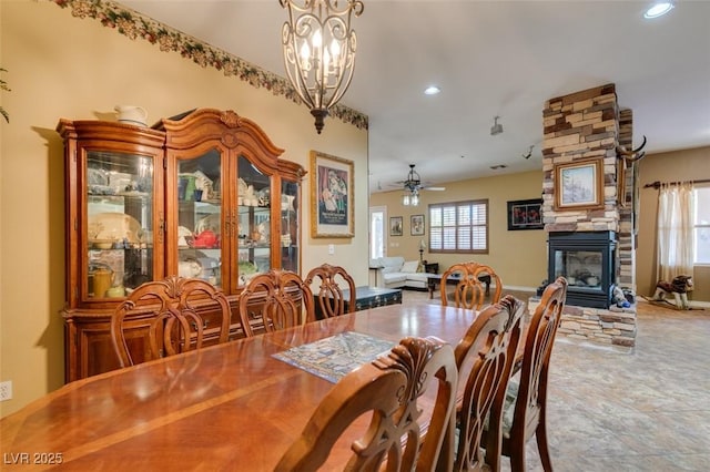 dining room with recessed lighting, ceiling fan with notable chandelier, and a stone fireplace