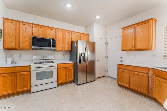 kitchen with appliances with stainless steel finishes, light countertops, light floors, a sink, and recessed lighting