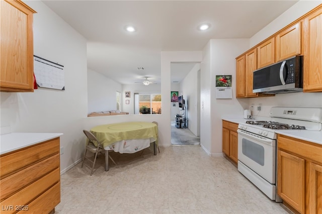 kitchen featuring white range with gas cooktop, stainless steel microwave, light countertops, light floors, and recessed lighting