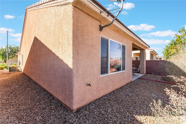 view of side of home with a patio area, fence, and stucco siding