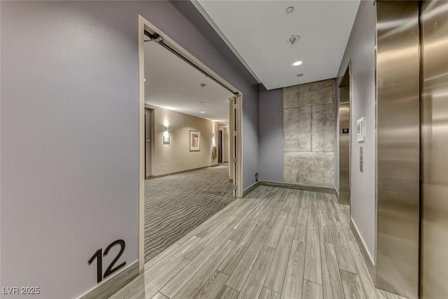 corridor featuring light wood-type flooring, elevator, and baseboards