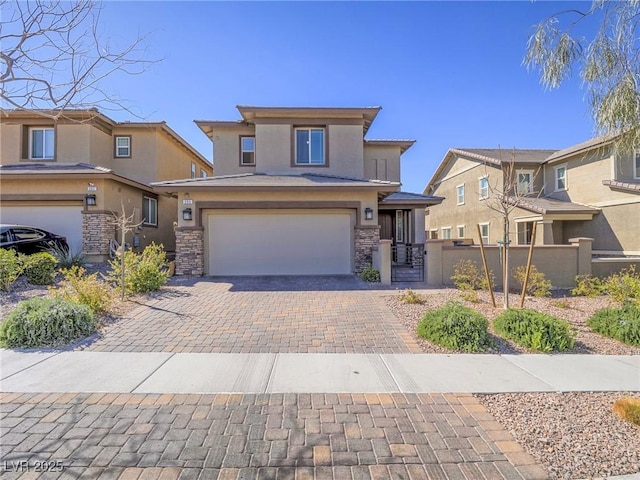 prairie-style home featuring stone siding, an attached garage, fence, decorative driveway, and stucco siding