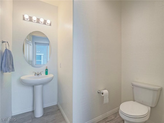 half bathroom featuring baseboards, a sink, toilet, and wood finished floors