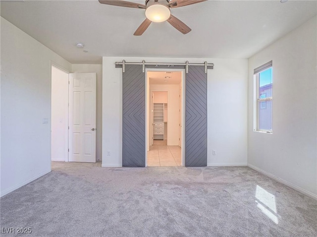 unfurnished bedroom featuring ceiling fan, a barn door, carpet flooring, and baseboards