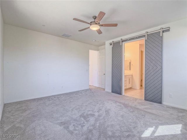 unfurnished bedroom featuring light carpet, a barn door, visible vents, ceiling fan, and ensuite bathroom