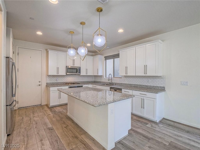 kitchen featuring stainless steel appliances, light wood-style flooring, decorative backsplash, white cabinets, and a sink