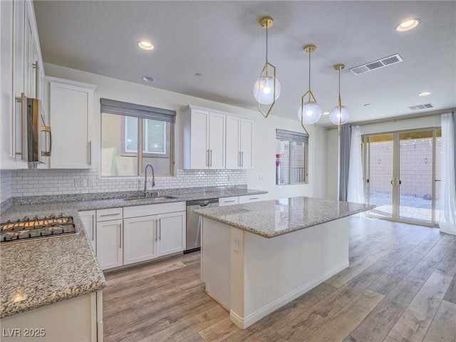 kitchen with stainless steel appliances, visible vents, light wood-style flooring, white cabinetry, and a sink