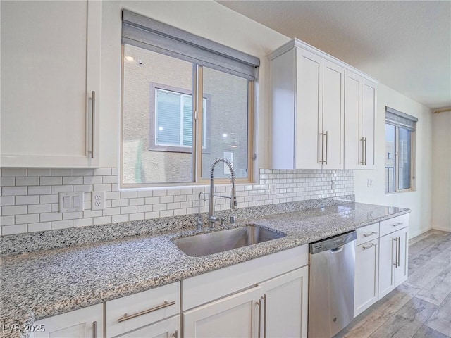 kitchen with a sink, white cabinetry, light wood-style floors, decorative backsplash, and dishwasher