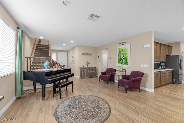 sitting room with light wood-style flooring, stairway, visible vents, and baseboards