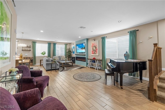 living area with light wood-style floors, stairs, visible vents, and a glass covered fireplace