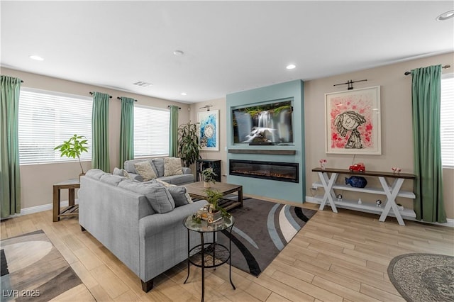 living area featuring wood finished floors, a glass covered fireplace, and recessed lighting