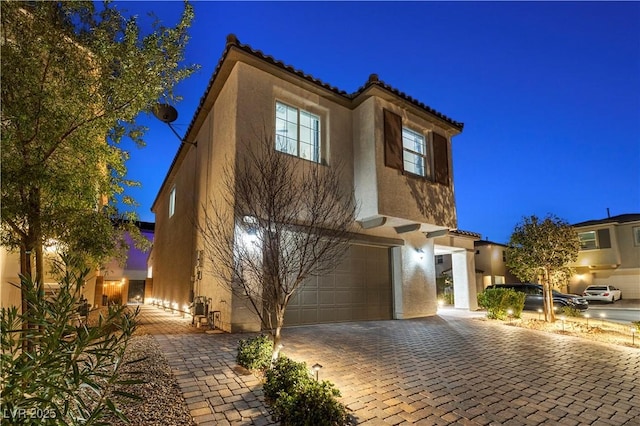 mediterranean / spanish-style home with a garage, decorative driveway, a tile roof, and stucco siding