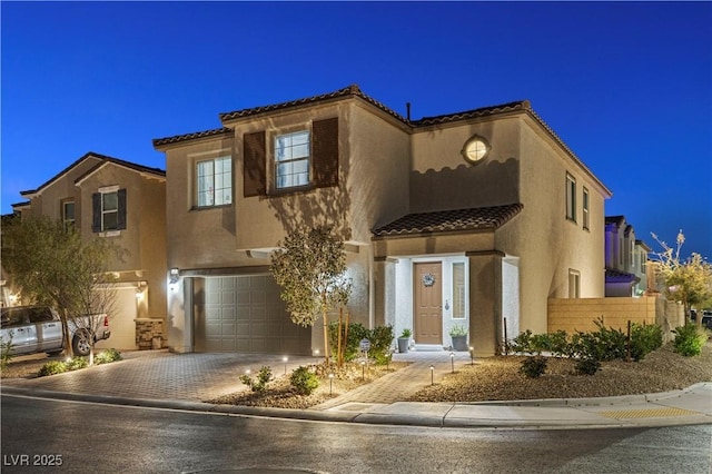 view of front of house with a garage, decorative driveway, fence, and stucco siding