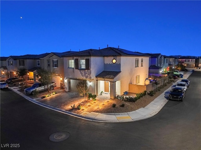 mediterranean / spanish home featuring a garage, a tiled roof, decorative driveway, a residential view, and stucco siding