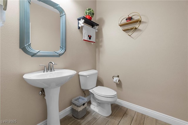 half bath with toilet, baseboards, and wood finish floors