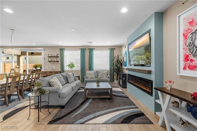 living room featuring a glass covered fireplace, wood finished floors, visible vents, and recessed lighting