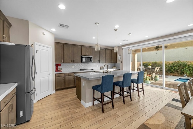 kitchen featuring visible vents, backsplash, appliances with stainless steel finishes, a sink, and a kitchen bar