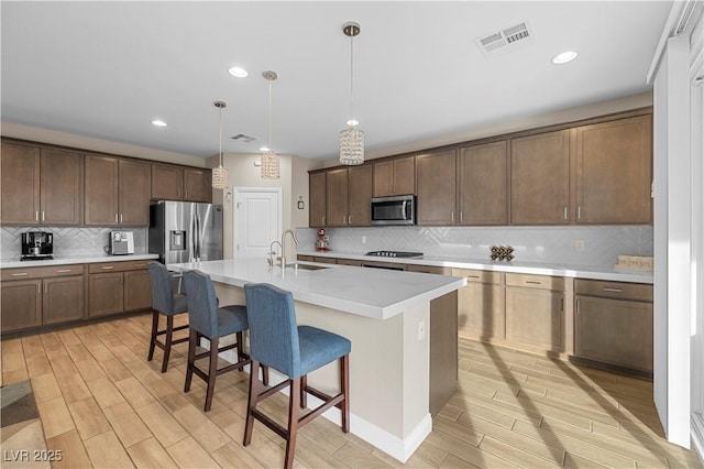 kitchen with visible vents, a kitchen breakfast bar, wood tiled floor, stainless steel appliances, and a sink