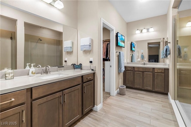 bathroom with two vanities, a sink, wood tiled floor, a stall shower, and a walk in closet