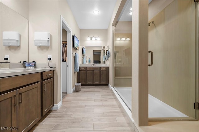 bathroom with a stall shower, a sink, wood tiled floor, a walk in closet, and two vanities