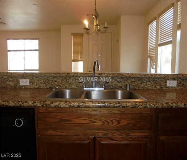 kitchen with black dishwasher, decorative light fixtures, an inviting chandelier, a sink, and light stone countertops