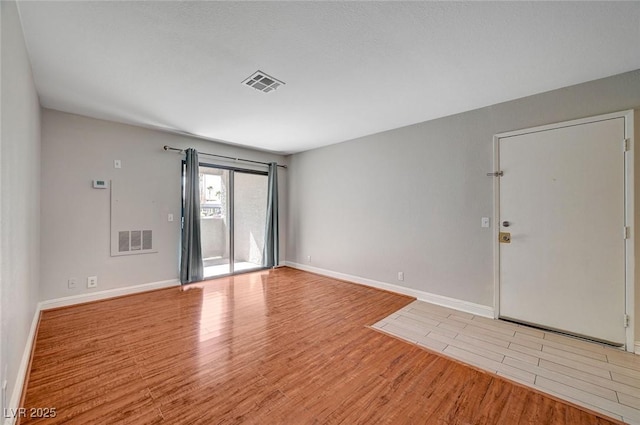 unfurnished room with wood finished floors, visible vents, and baseboards