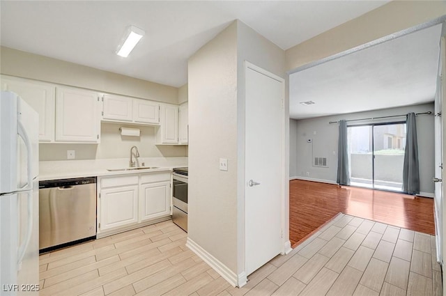 kitchen with stainless steel appliances, wood finish floors, a sink, white cabinetry, and light countertops