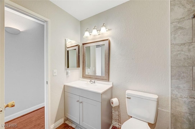 bathroom with baseboards, a textured wall, toilet, wood finished floors, and vanity