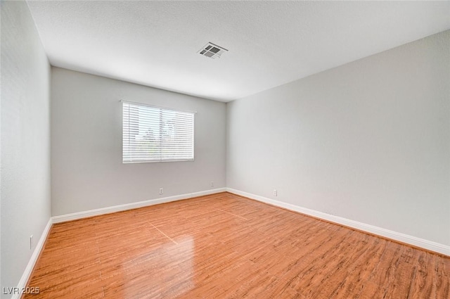 unfurnished room with baseboards, a textured ceiling, visible vents, and wood finished floors