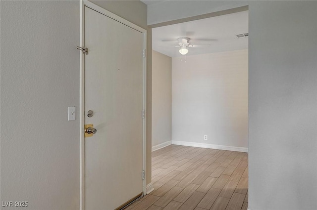 empty room featuring a ceiling fan, visible vents, baseboards, and wood finished floors