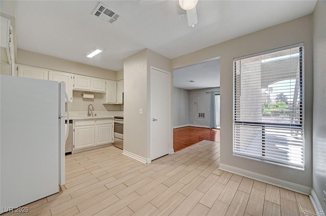 kitchen with light wood finished floors, visible vents, stove, freestanding refrigerator, and a sink