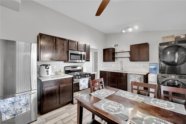 kitchen with open shelves, stainless steel appliances, stacked washer and dryer, a sink, and dark brown cabinetry