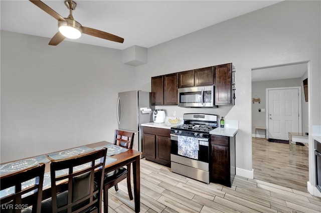 kitchen featuring a ceiling fan, appliances with stainless steel finishes, light countertops, dark brown cabinets, and wood finish floors