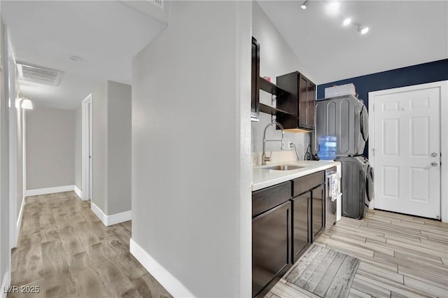 kitchen featuring a sink, dark brown cabinetry, visible vents, and stacked washer / dryer