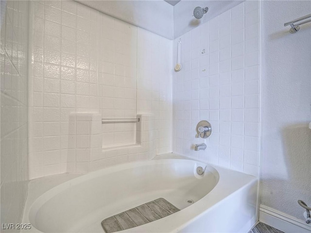 full bath featuring a textured wall, shower / bathing tub combination, and baseboards