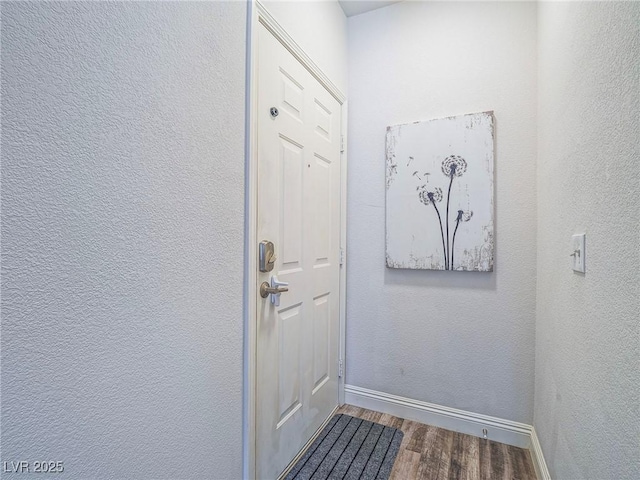 doorway featuring a textured wall, wood finished floors, and baseboards