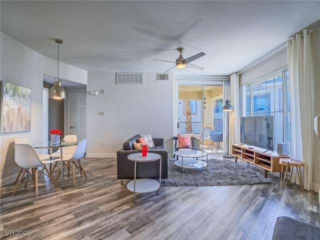 living area featuring visible vents, a textured ceiling, baseboards, and wood finished floors