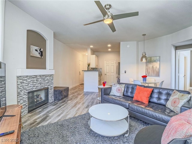 living area with a ceiling fan, recessed lighting, light wood-style flooring, and a tiled fireplace