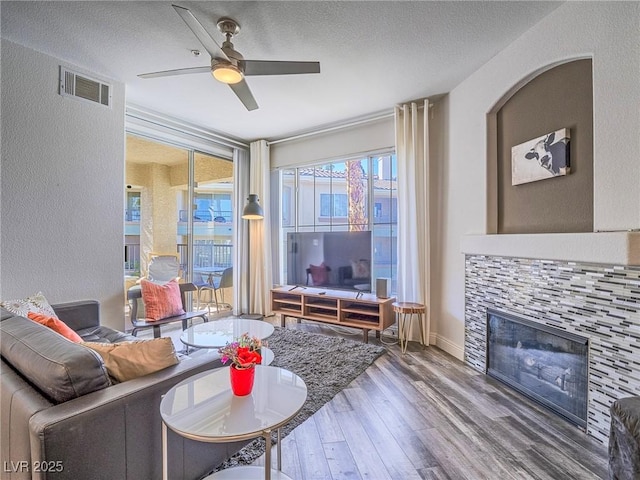 living area featuring visible vents, ceiling fan, wood finished floors, a textured ceiling, and a fireplace