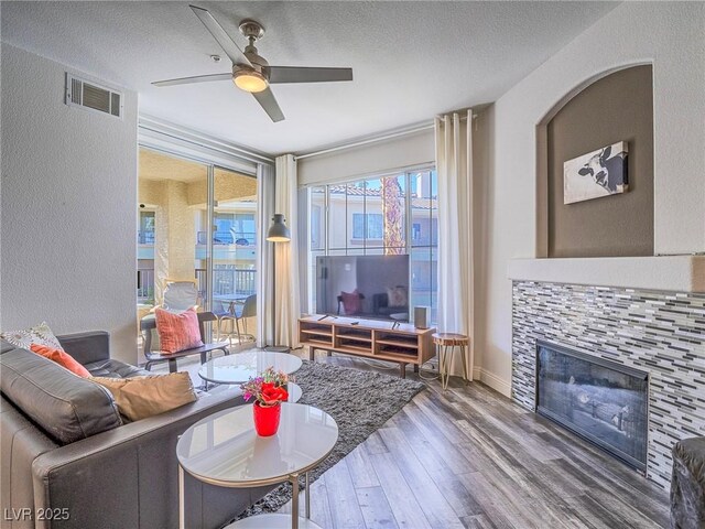 7111 S Durango Dr Unit 305, Las Vegas, NV 89113 - living room featuring wood finished floors, a ceiling fan, a tile fireplace, a textured wall, and a textured ceiling