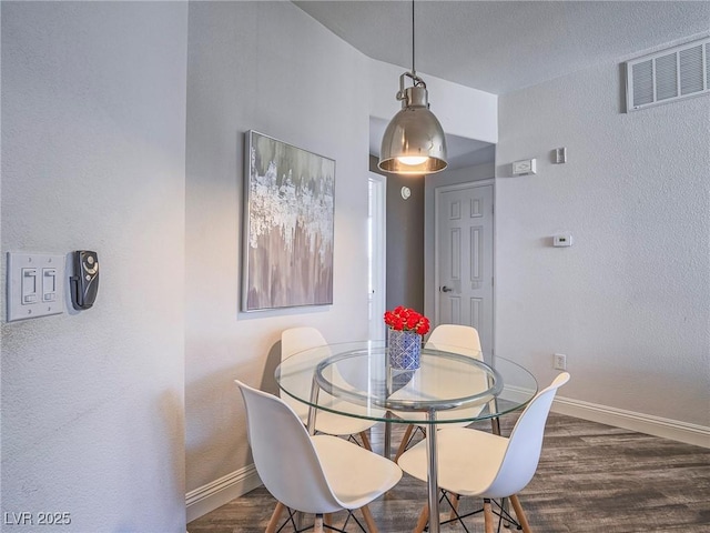 dining room featuring a textured wall, wood finished floors, visible vents, and baseboards