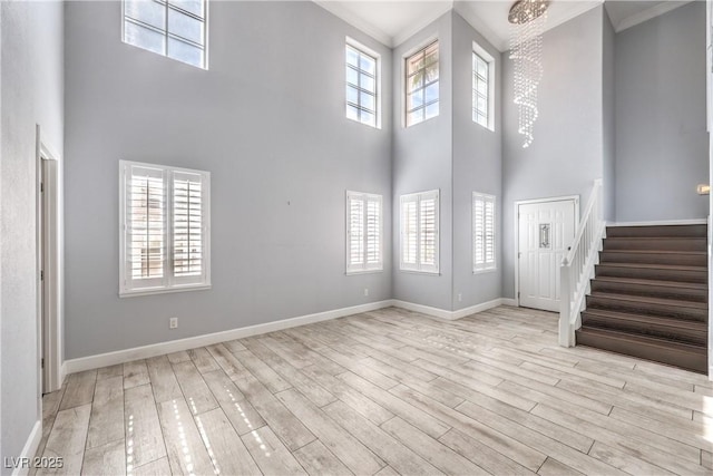 unfurnished living room with a chandelier, wood finished floors, baseboards, ornamental molding, and stairway