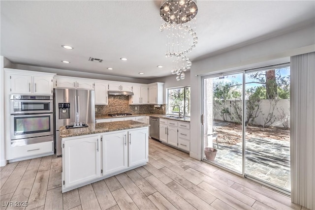 kitchen with under cabinet range hood, appliances with stainless steel finishes, visible vents, and white cabinets