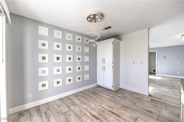 unfurnished room with light wood-type flooring, visible vents, baseboards, and a notable chandelier