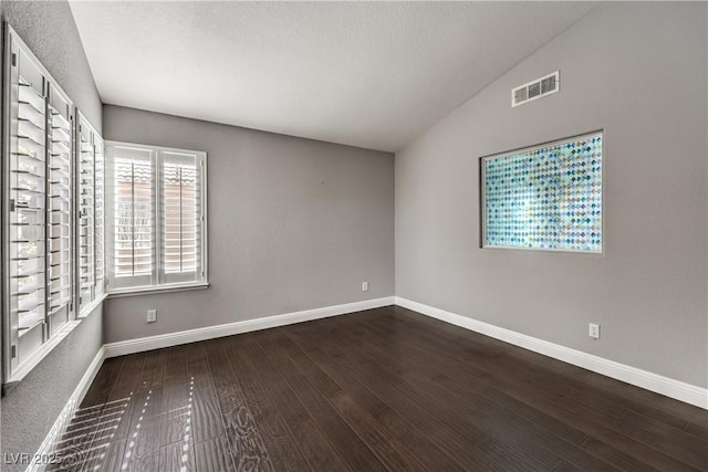 spare room with vaulted ceiling, wood finished floors, visible vents, and baseboards