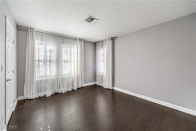 spare room with dark wood-style floors, visible vents, and baseboards