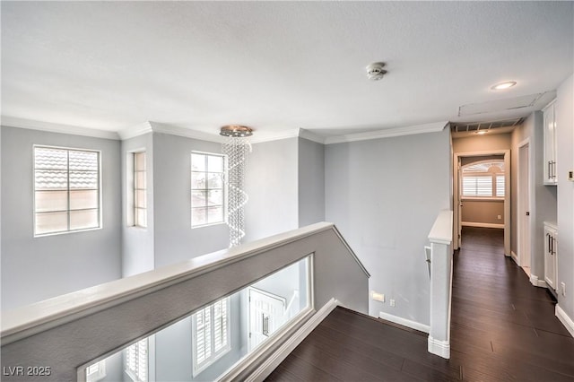 hallway featuring dark wood-style flooring, baseboards, crown molding, and an upstairs landing